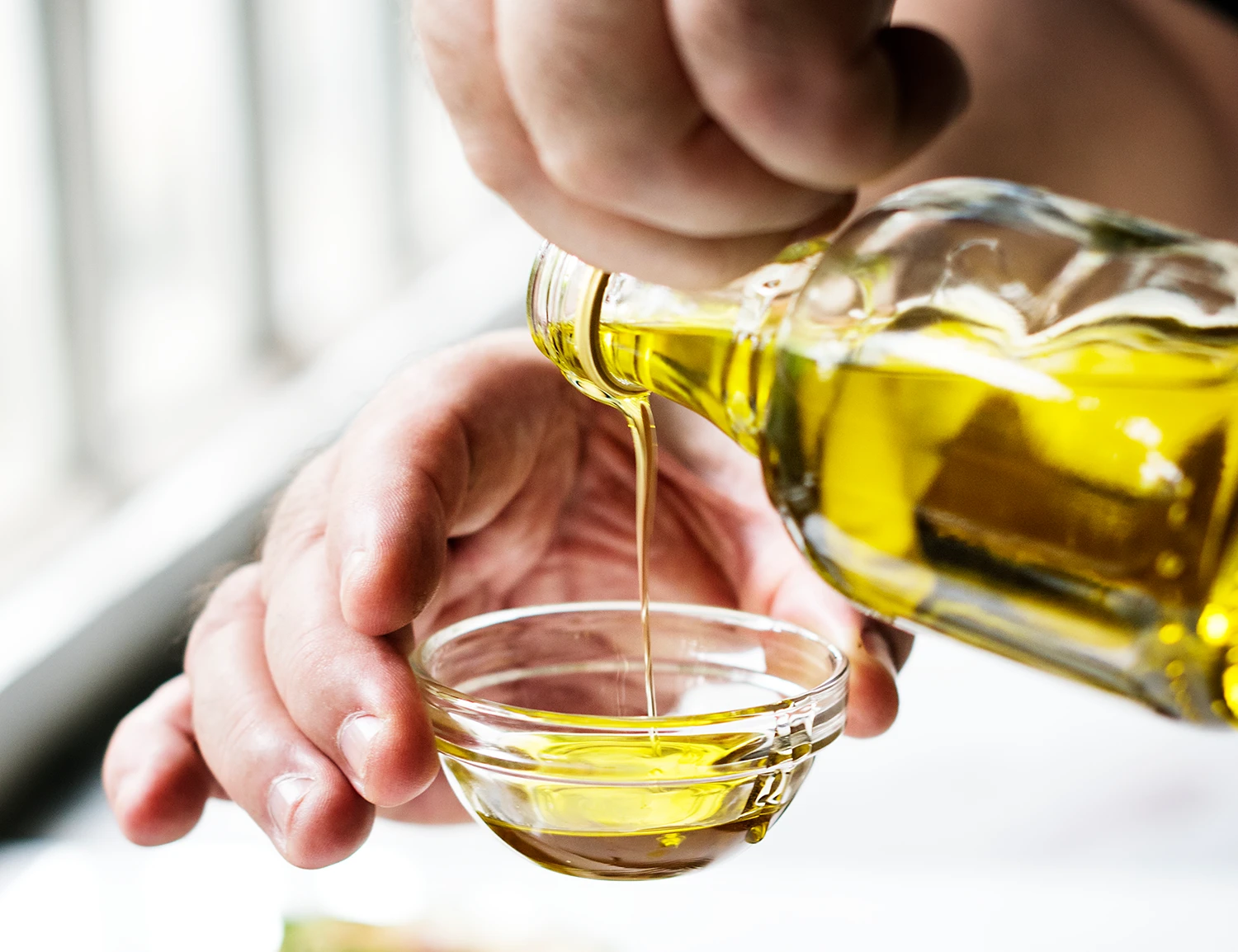 Natives Olivenöl extra wird aus der Flasche in ein kleines Glasschälchen gegossen, um es zu verkosten